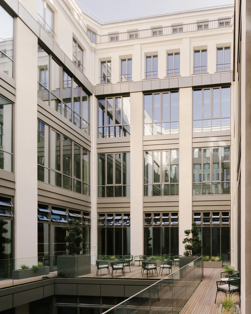 Interior courtyard with glazed facades, horizontal banding, planted beds, and seating on a wooden deck
