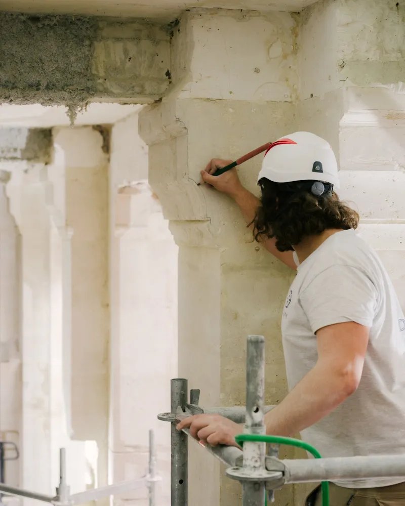 Worker in hardhat marking measurements on a concrete column with red pencil