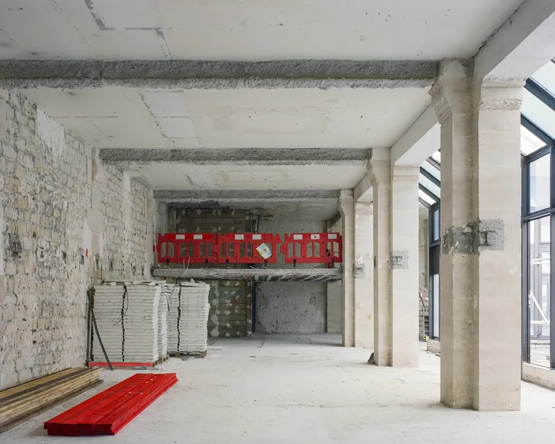 Interior space with exposed brick wall, concrete beams and red safety barriers on mezzanine