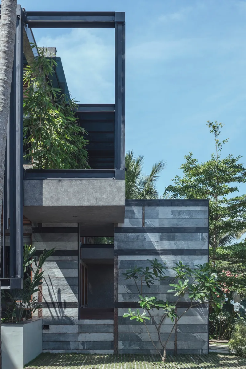 Exterior view of striped stone facade with cantilevered steel frame and vertical greenery beneath a clear sky
