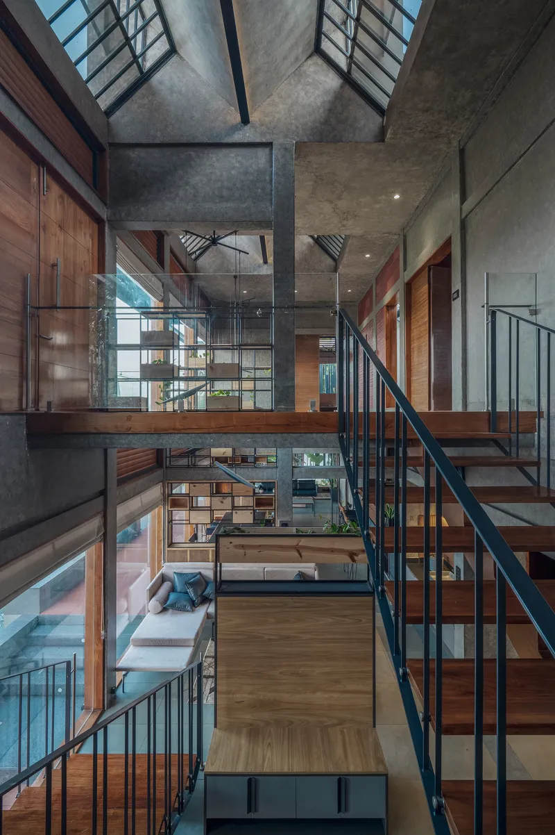 Double-height interior void with timber and steel stairs connecting stacked platforms under concrete ceiling
