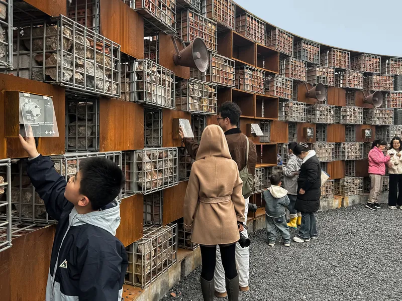 Families examining display niches set into the gabion and corten steel grid wall along the gravel plaza