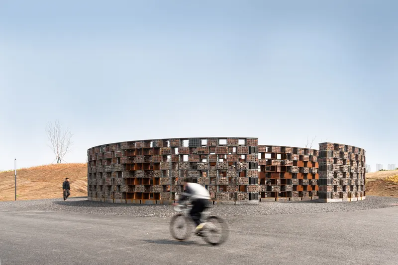Cylindrical brick pavilion with a patterned facade beside a gravel path as a cyclist passes