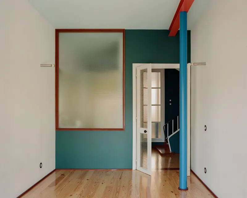 Room corner showing teal accent wall, red-framed translucent glass panel, and cylindrical blue column
