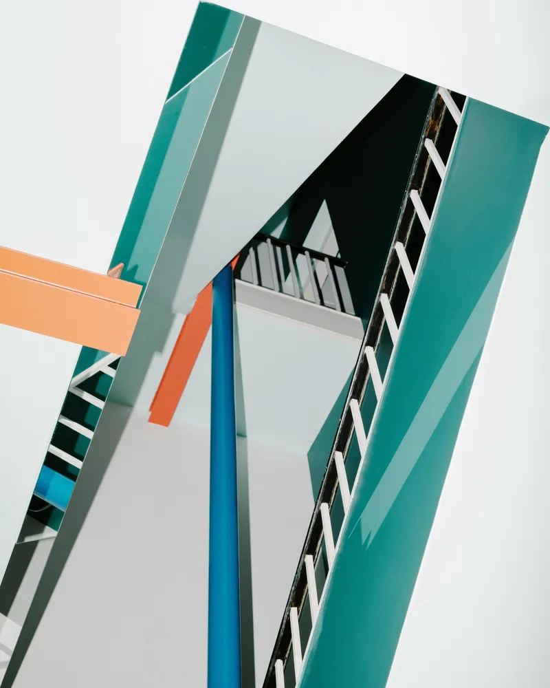 Looking up through the stairwell void with teal, orange, and blue painted beams and railings