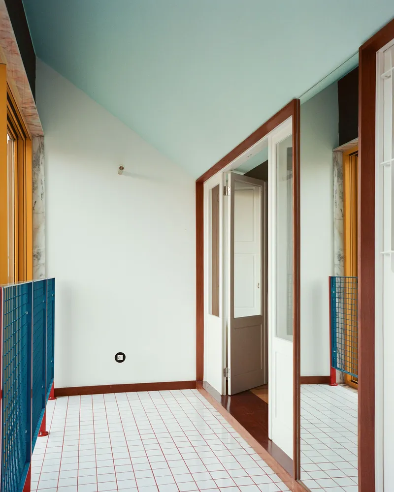 Interior corridor with white tile floor, teal ceiling, red timber doorframes, and glass block panels