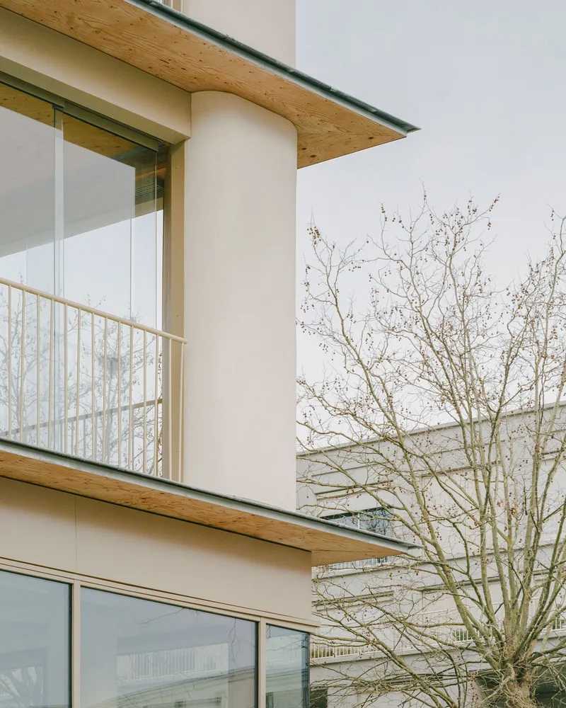 Close-up of stacked timber balconies with white stucco walls and a bare tree in winter