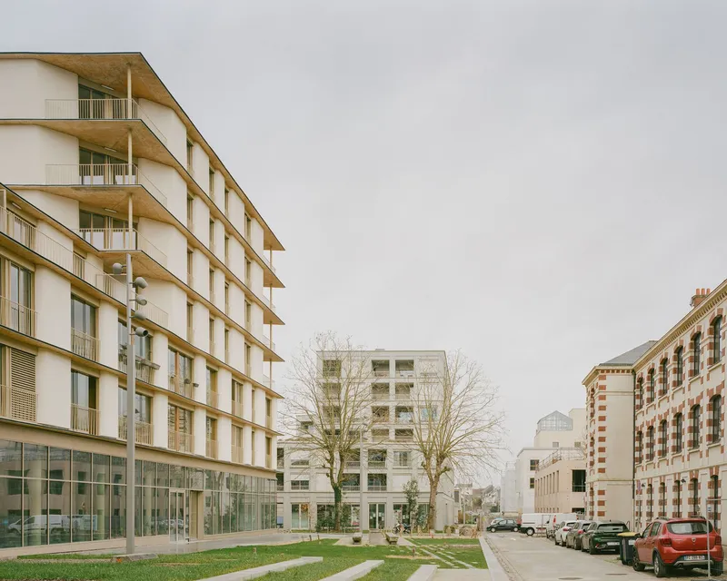 Residential blocks with timber and white facades surrounding a central lawn and courtyard under overcast sky