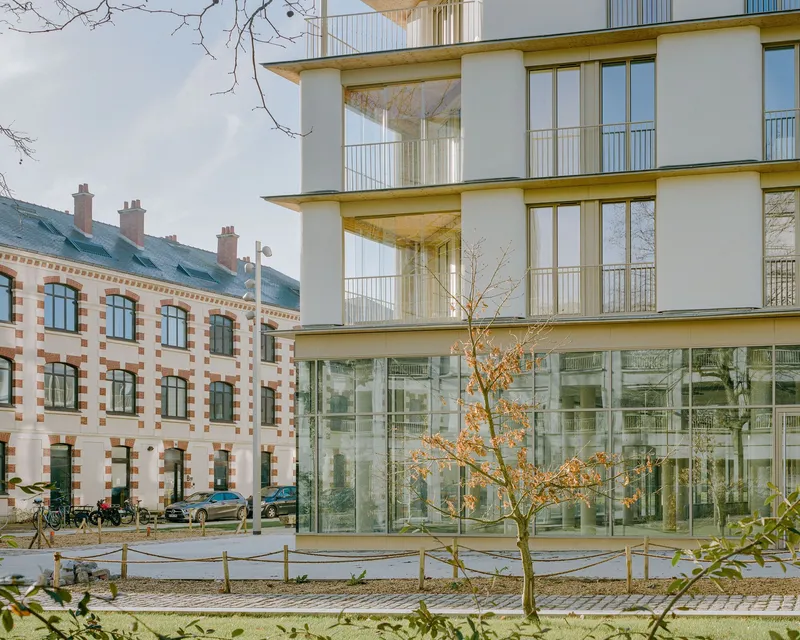 Ground floor glass curtain wall beneath upper residential levels with cylindrical columns and bare tree