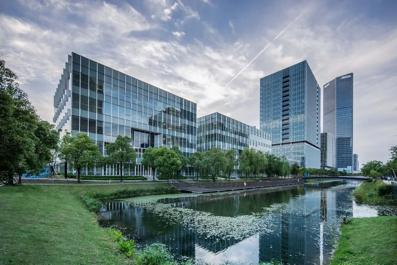 Glass office towers reflected in a landscaped pond with lily pads at dusk