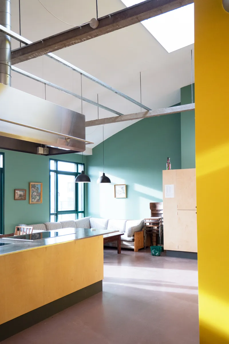 Open-plan living space with exposed timber beam, yellow column, and teal wall in bright daylight