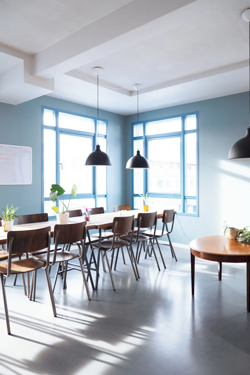 Dining room with pale blue walls, timber chairs, and pendant lamps casting shadows across polished concrete floor