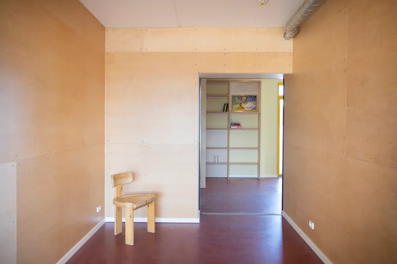 Plywood-clad room with dark resin floor and doorway to built-in shelving beyond