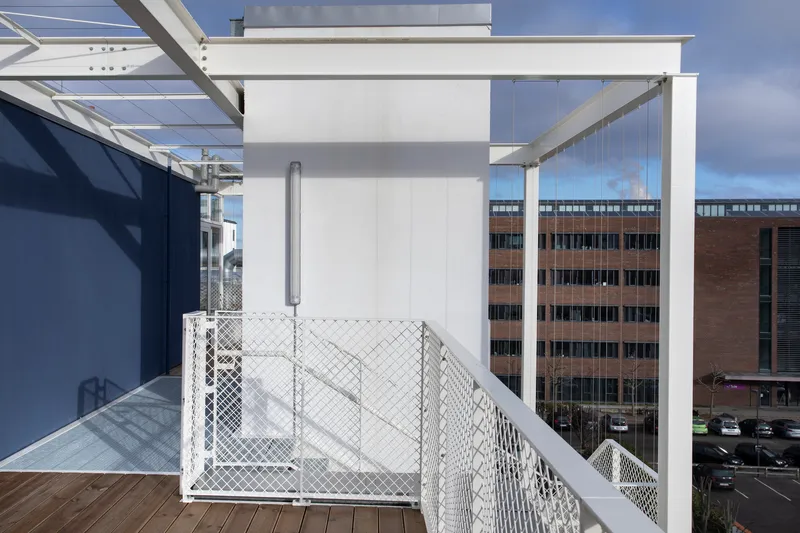 Rooftop terrace with white pergola structure and mesh safety railing overlooking neighboring brick buildings