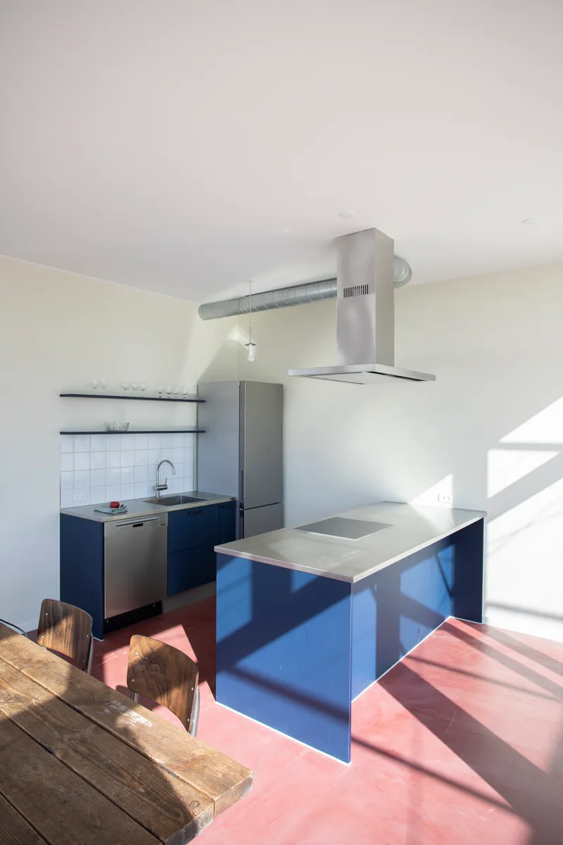 Compact kitchen with navy blue cabinetry and pink flooring in bright afternoon sunlight