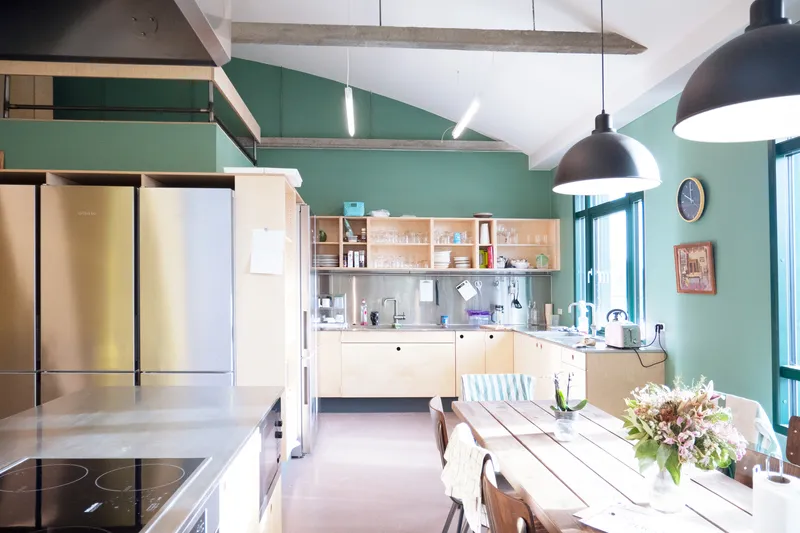 Shared kitchen with green walls, pendant lamps, and exposed concrete beams at the ceiling