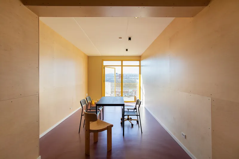 Interior room with plywood walls, yellow window frames, and dark resin floor beneath white ceiling