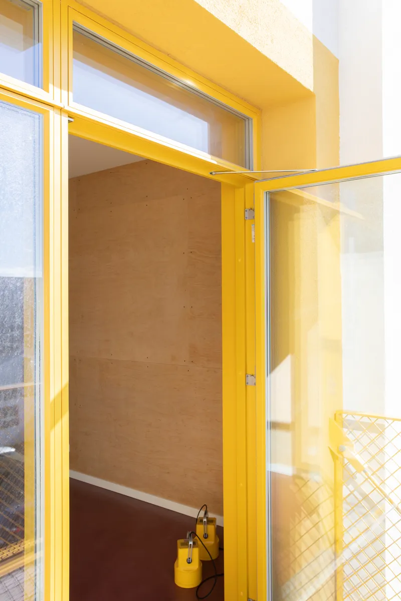 Yellow-framed door and window assembly with plywood panel and mesh railing visible outside