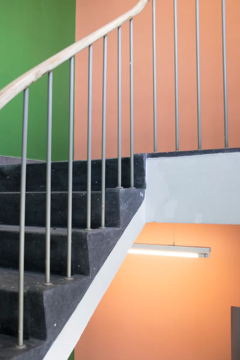 Concrete staircase with white pipe railings ascending past green and peach-painted walls