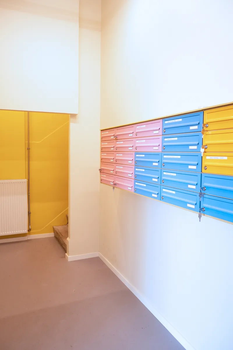 Entry hall with wall-mounted mailboxes in yellow, pink and blue beside a yellow door