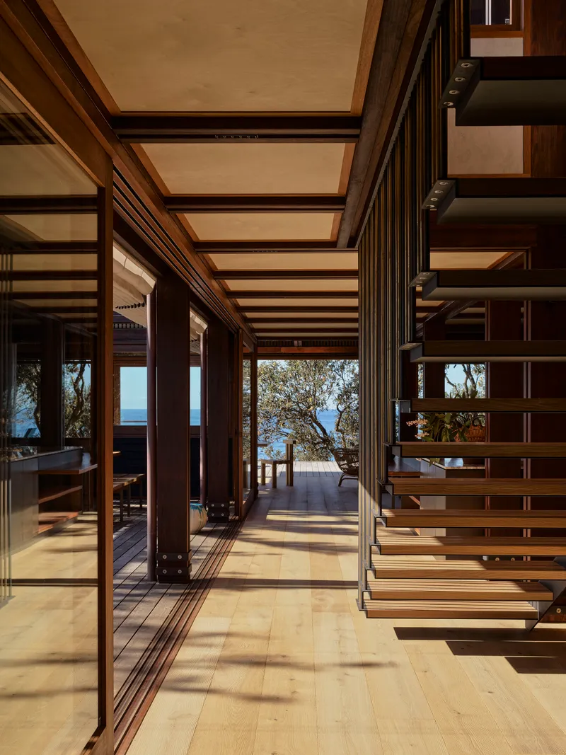 Open-tread timber stair beside folding glass doors leading to a deck with ocean horizon