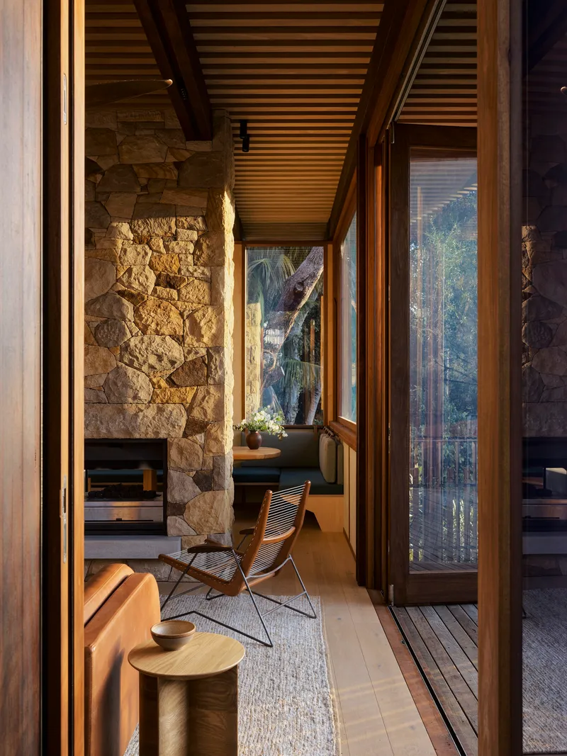 Narrow reading nook with stone wall, timber chair and glazed doors framing garden beyond