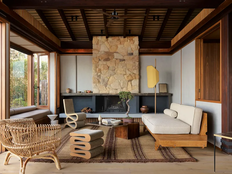 Living room with exposed timber ceiling beams and rough stone fireplace surround facing floor-to-ceiling windows