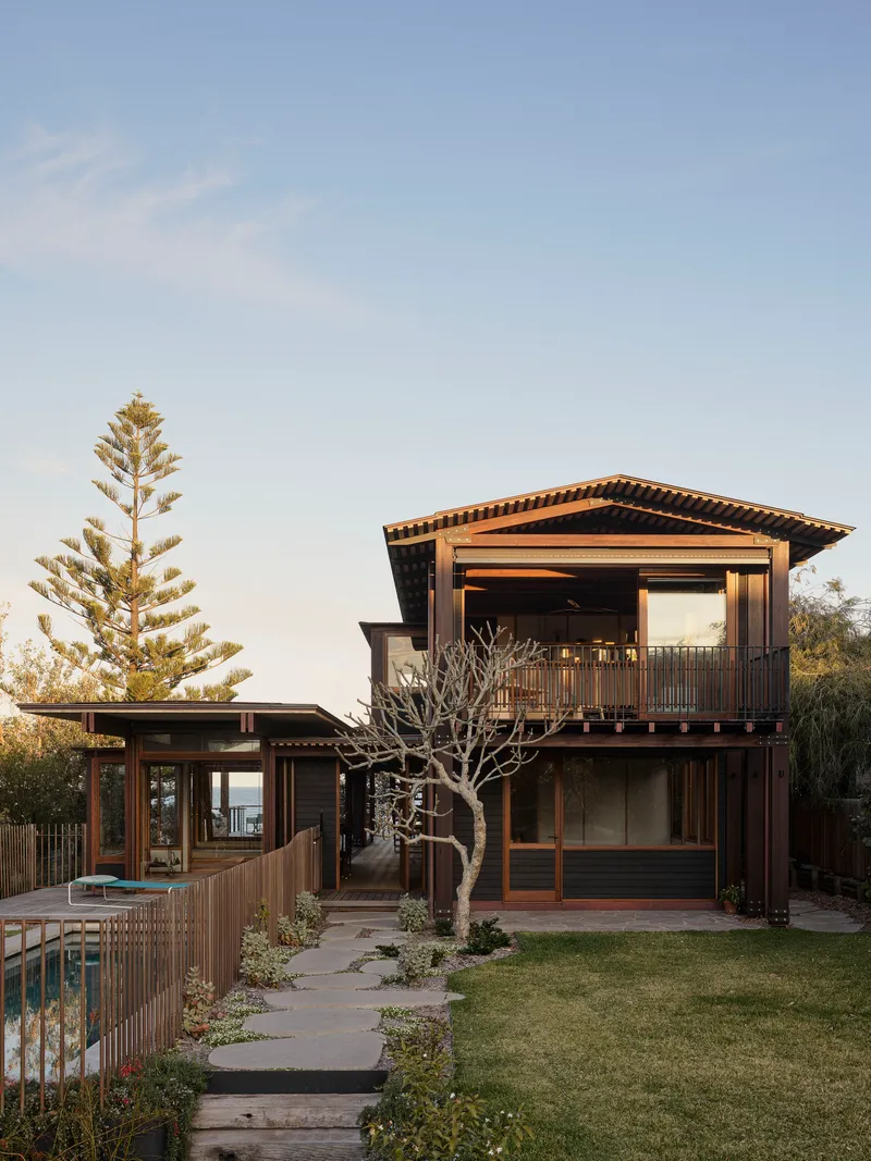 Garden view of timber-framed volumes with deep overhangs and a bare tree in the lawn