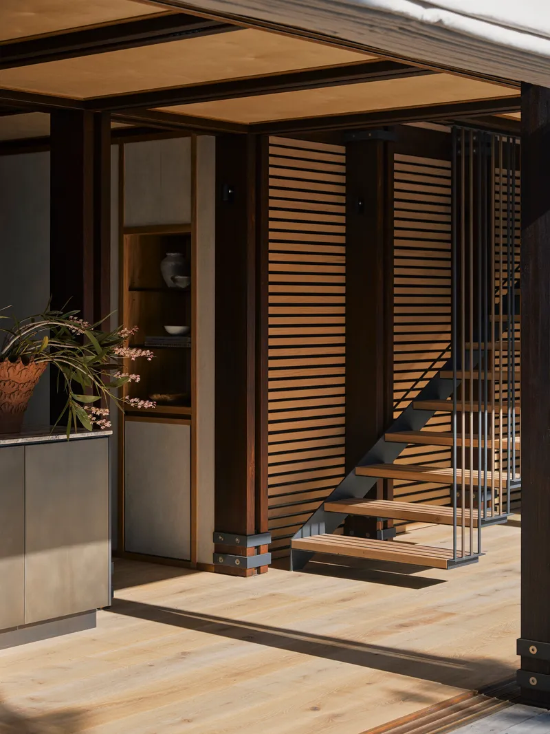 Open timber-framed threshold with horizontal slatted screens flanking a steel and wood staircase
