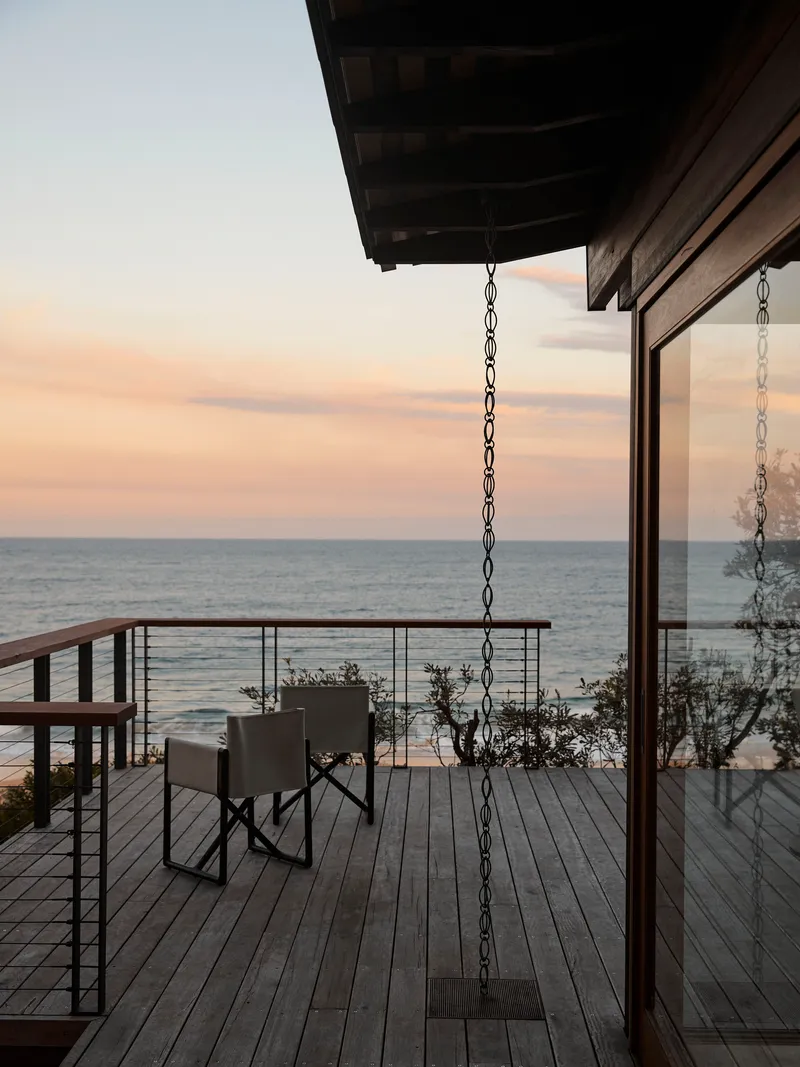 Timber deck with chain-suspended bench facing the ocean at dusk with glass sliding doors