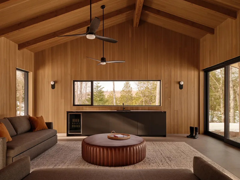 Living room with exposed timber rafters, horizontal wood paneling, and horizontal window framing forest views