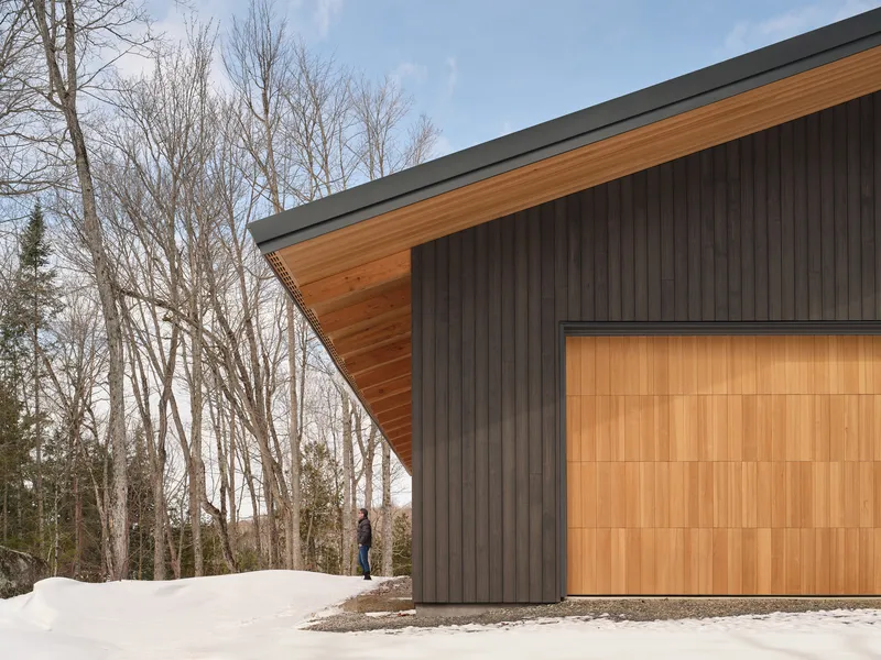 Corner detail showing the timber soffit overhang meeting dark vertical siding and wood-paneled garage door