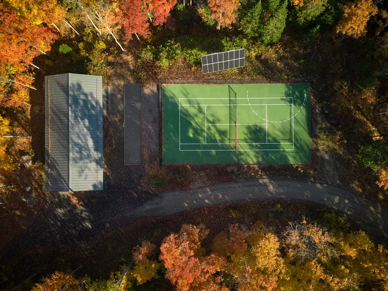 Aerial view of a green sport court and timber pavilion surrounded by autumn foliage