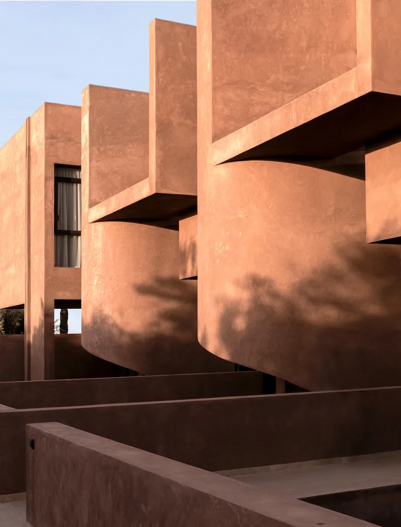 Stepped rammed earth volumes and cantilevered slabs casting shadows in afternoon sunlight