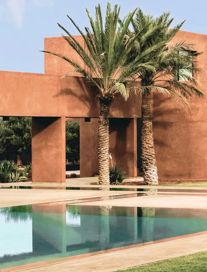 Palm tree reflected in the still turquoise pool alongside the rammed earth colonnade