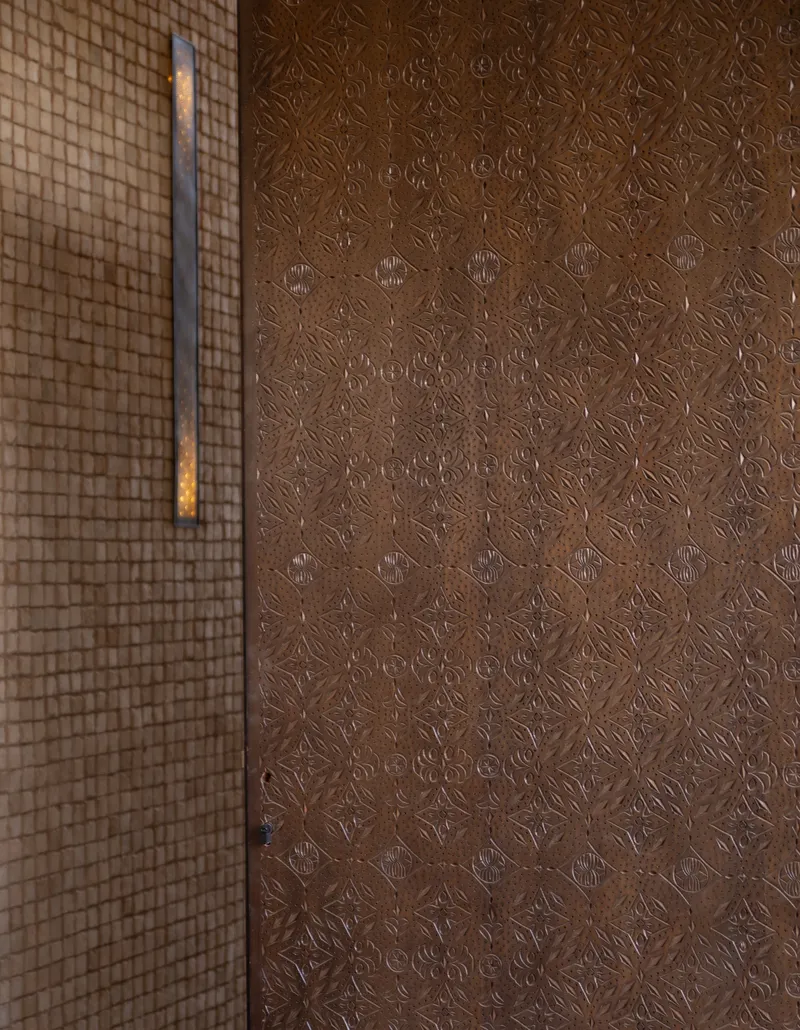 Embossed metal door panel with geometric pattern beside a gridded screen wall in low light