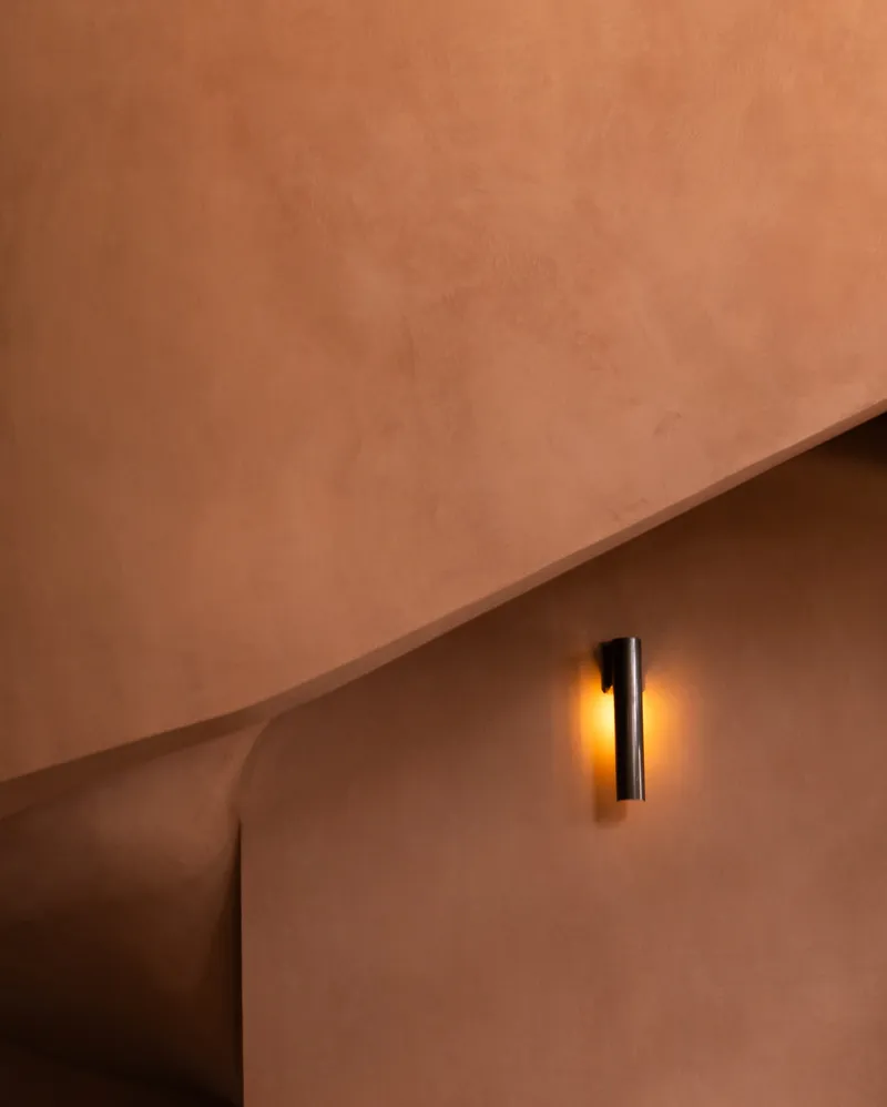 Cylindrical wall sconce casting golden light on a curved plaster wall above a rounded opening