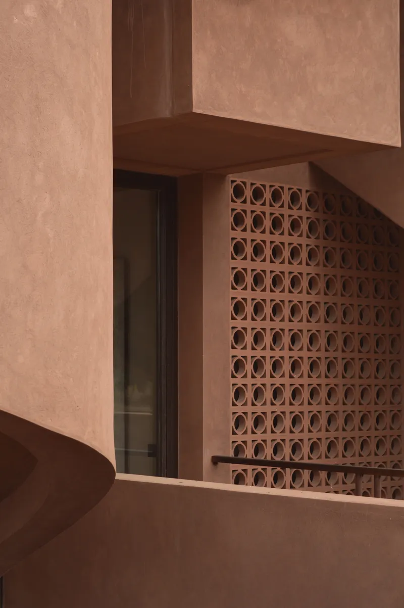Terracotta breeze block screen beside a dark timber doorway beneath a plastered beam