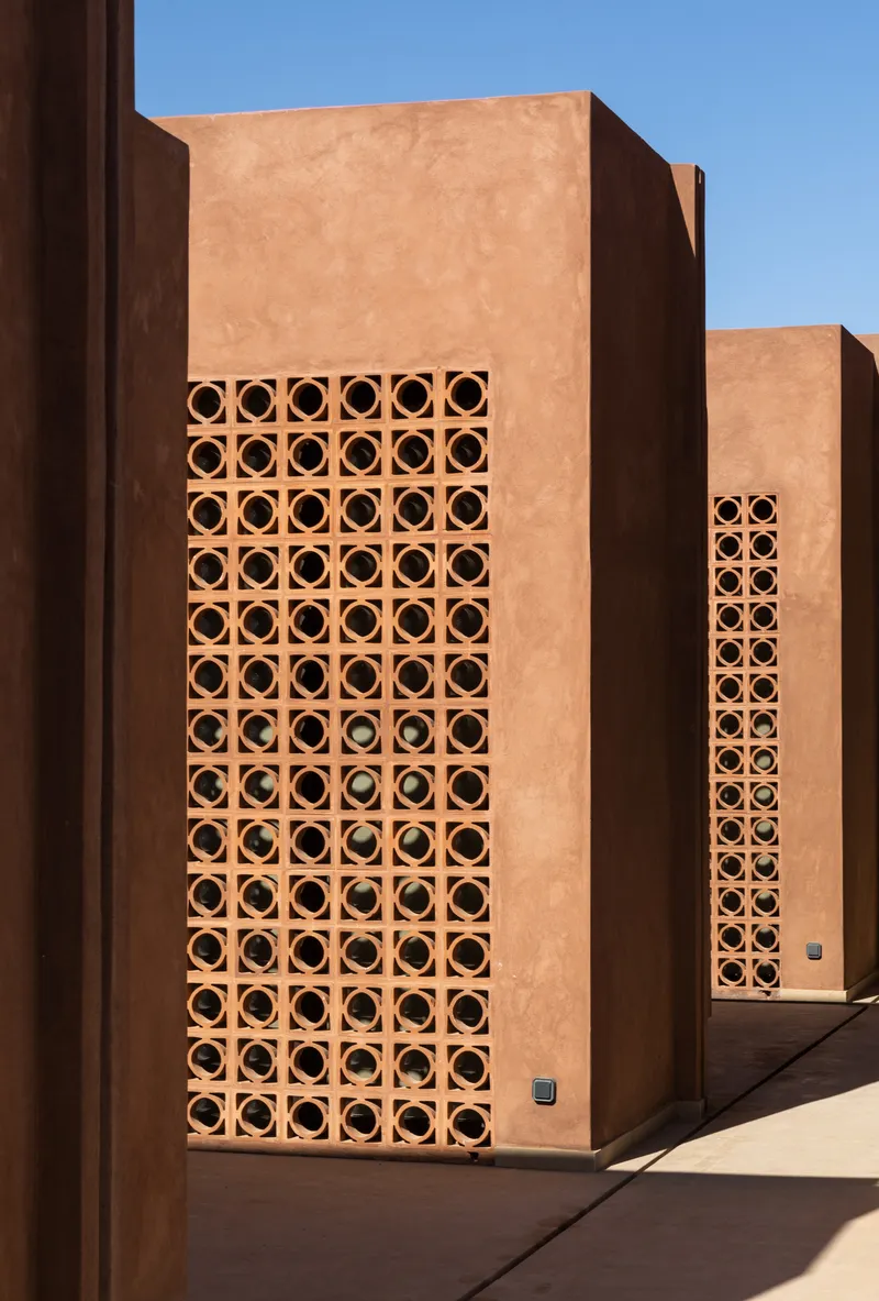 Exterior facade with tall terracotta breeze block panels set into earthen plaster volumes under blue sky