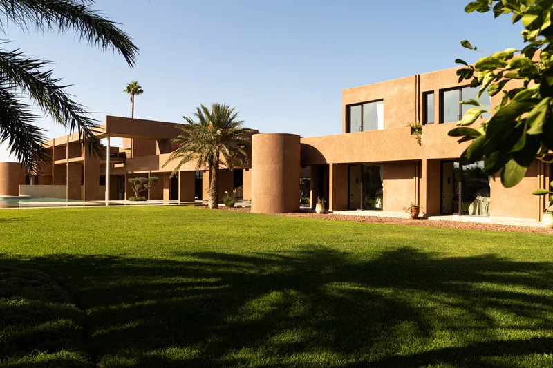 Garden view across the lawn showing cylindrical and cubic terracotta volumes framed by palm trees