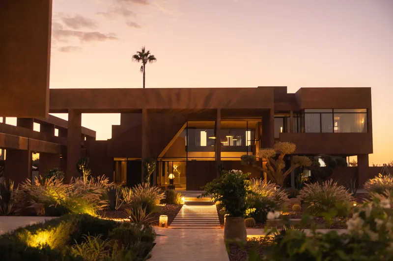 Terraced pathway with planted beds leading to the illuminated multi-level residence at dusk