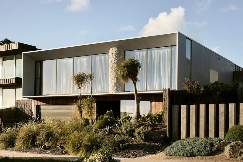 Street view of the two-story facade with white curtained glazing and planted forecourt with palms and grasses