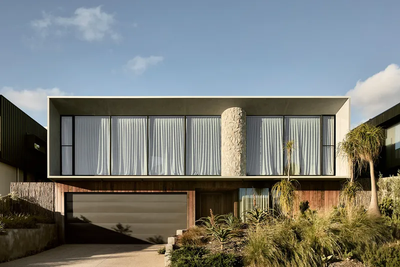 Front elevation showing the concrete upper volume with draped curtains above a timber-clad garage and driveway
