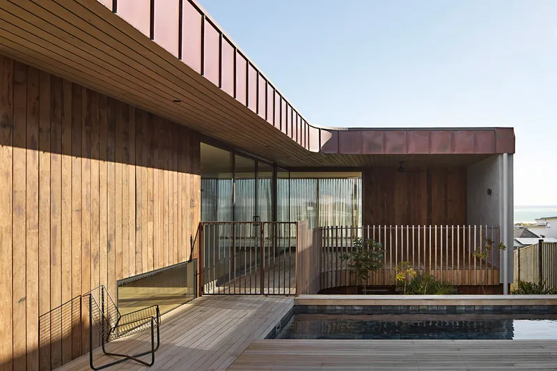 Rear terrace with timber deck and pool surrounded by blonde wood cladding and pink metal panels
