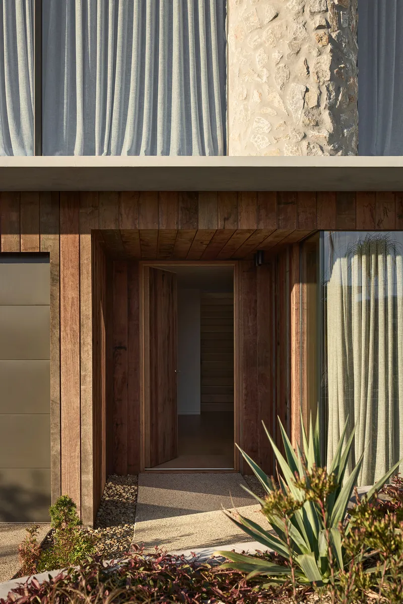 Front entry porch with vertical timber cladding, exposed rafters, and succulents in afternoon sunlight
