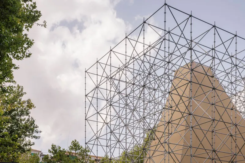 Detail of the steel truss framework rising against a cloudy sky with tree branches visible