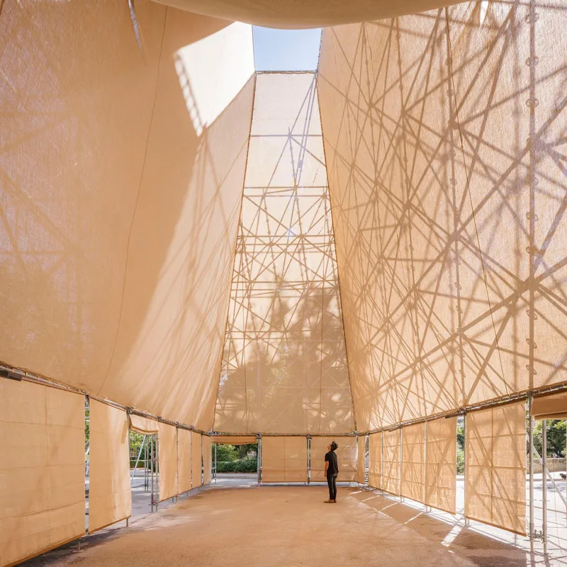 Interior view showing fabric-clad walls converging toward a square roof opening with a visitor standing inside