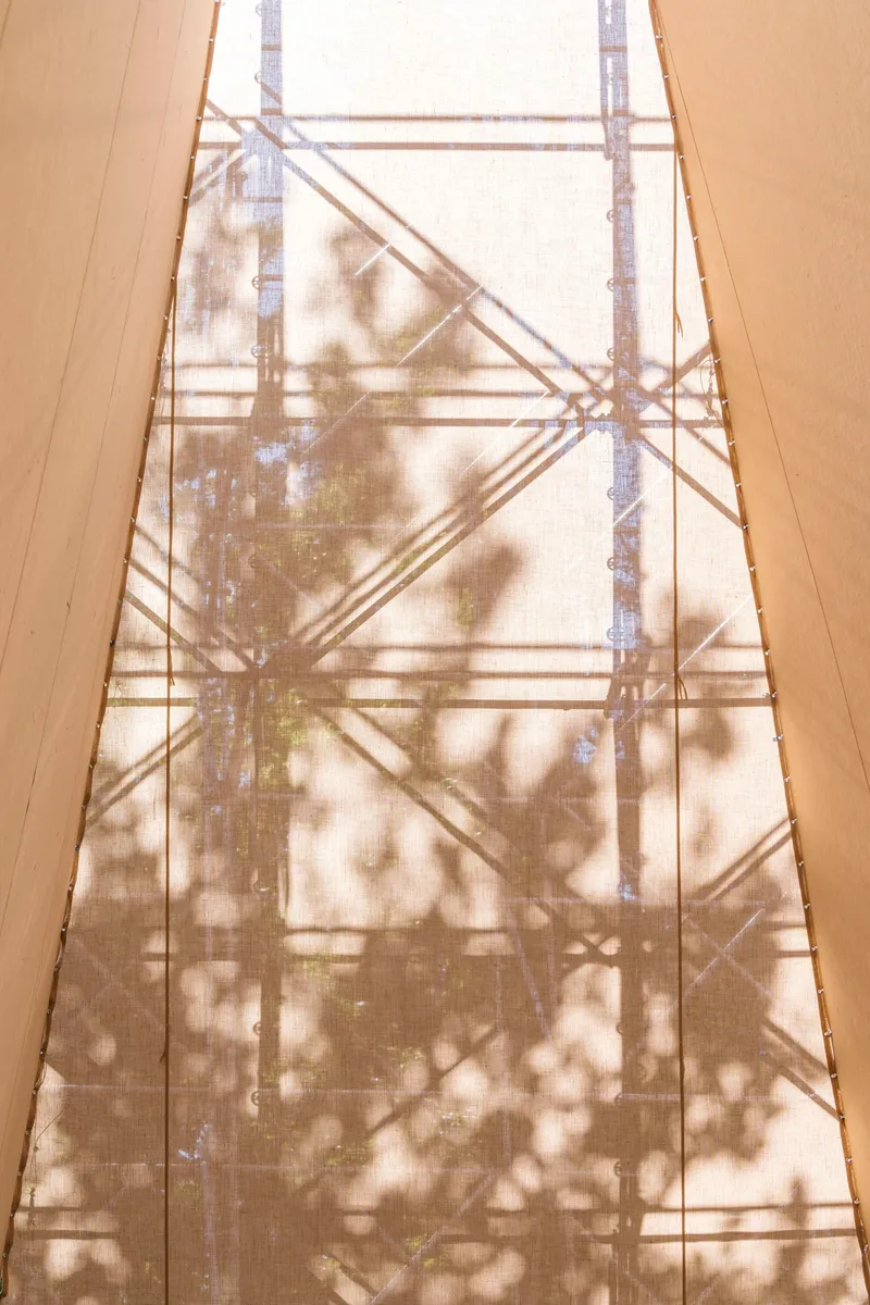 Scaffold shadows cast onto woven fabric panels illuminated by filtered daylight from above
