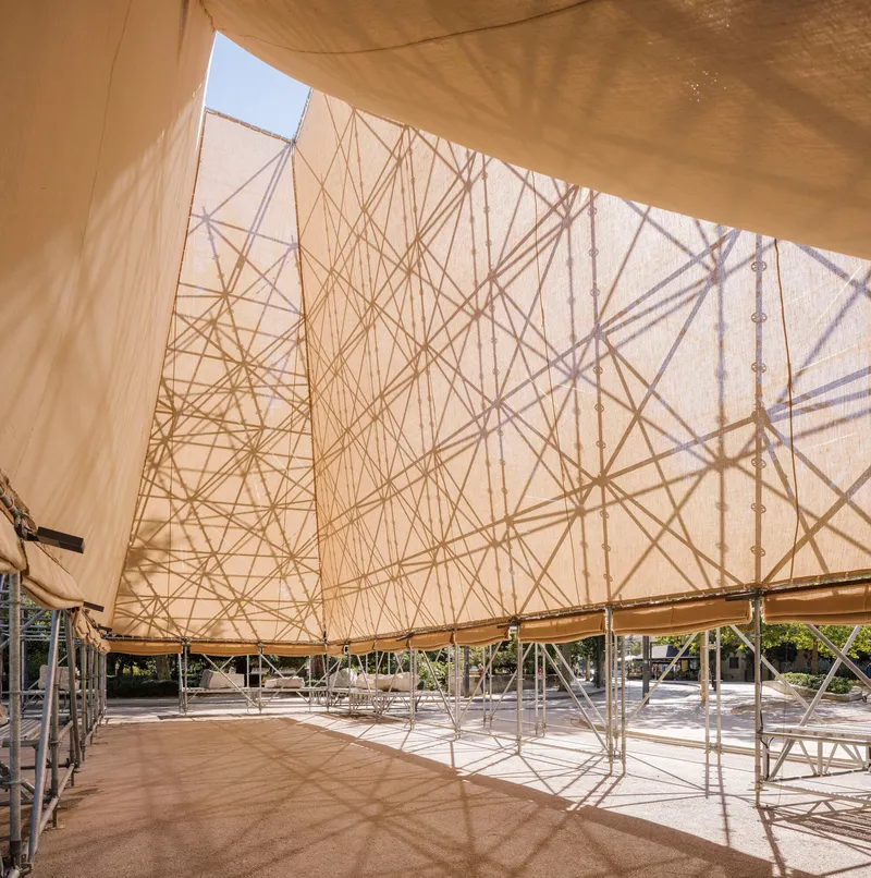 Fabric canopy interior showing triangulated cable patterns casting shadows on the translucent membrane in daylight