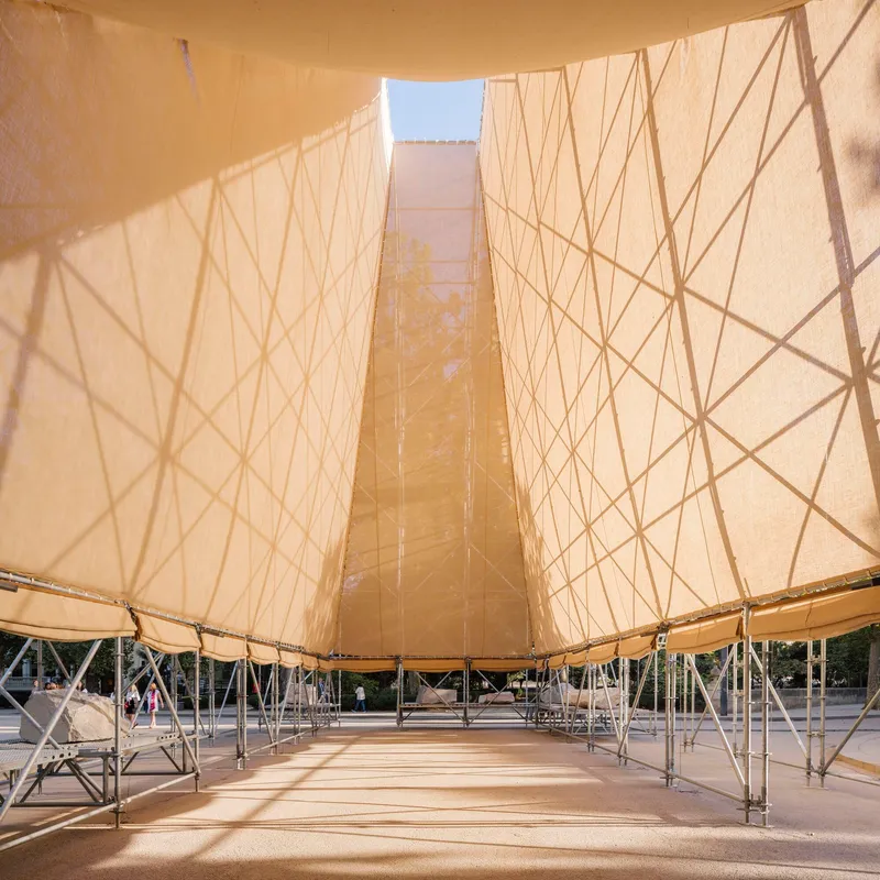 View under the tented roof with sunlight filtering through the fabric and scaffold framework below